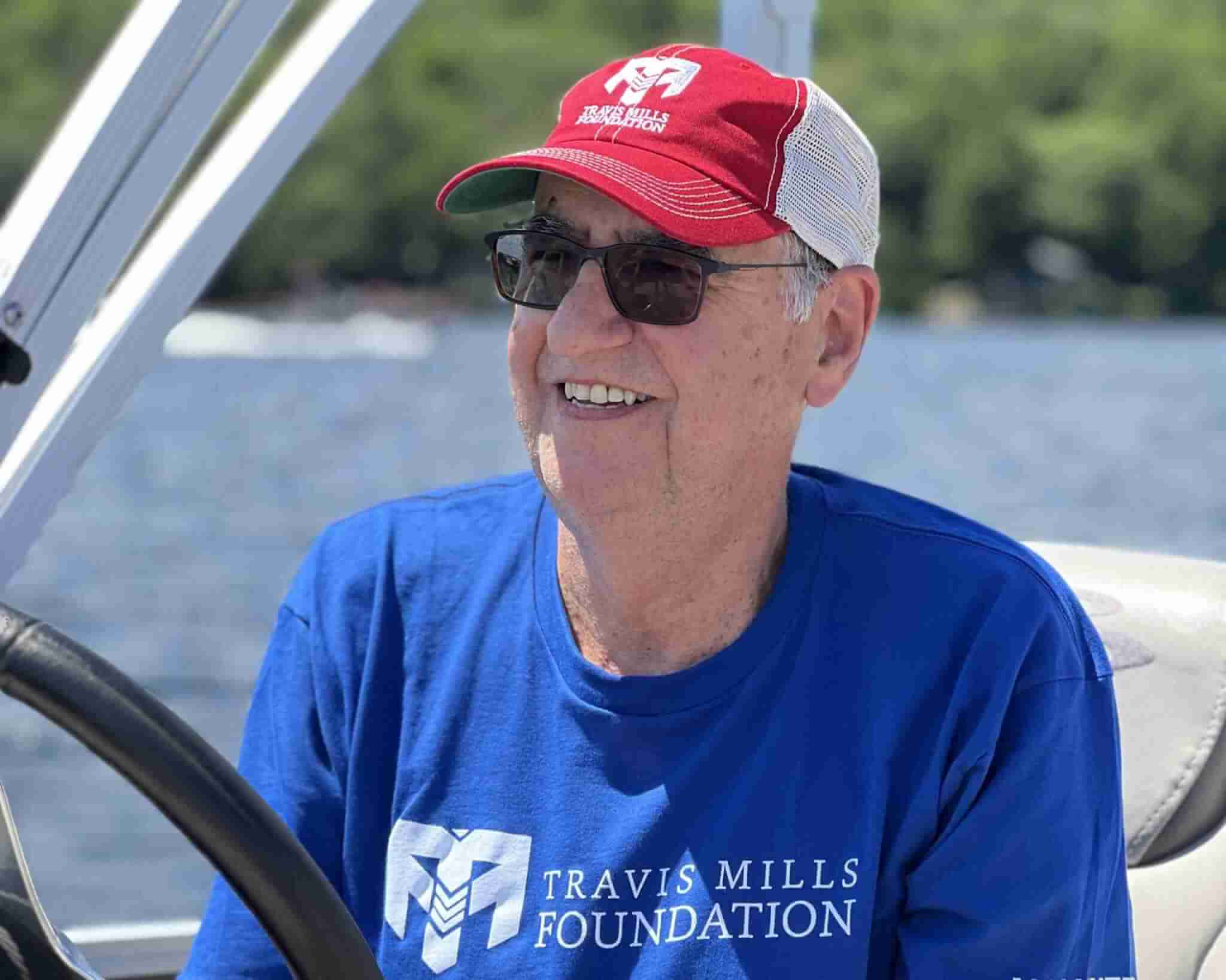 Older gentleman with Travis Mills Foundation apparel driving a motor boat